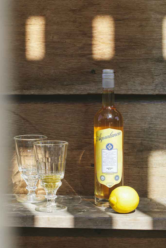 Flasche Aqualanca L'Anis d'Antan mit zwei Gläsern und einer Zitrone auf einem Holztisch