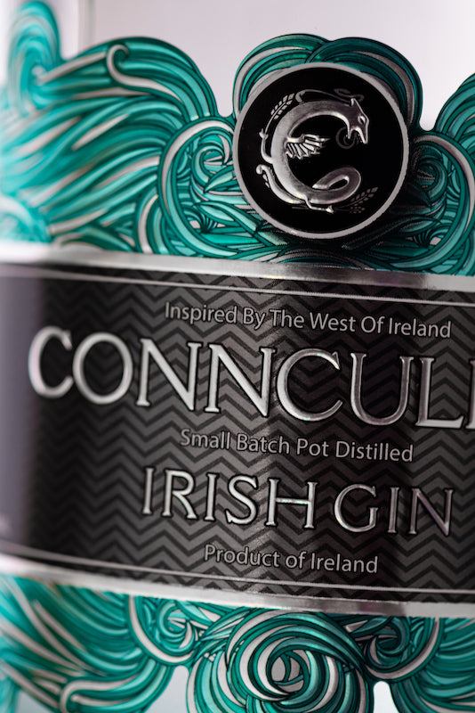 Nahaufnahme des Conncullin Irish Gin Etiketts mit silbernem Schriftzug, türkisfarbenen Wellen und schwarzem Emblem der Connacht Distillery.