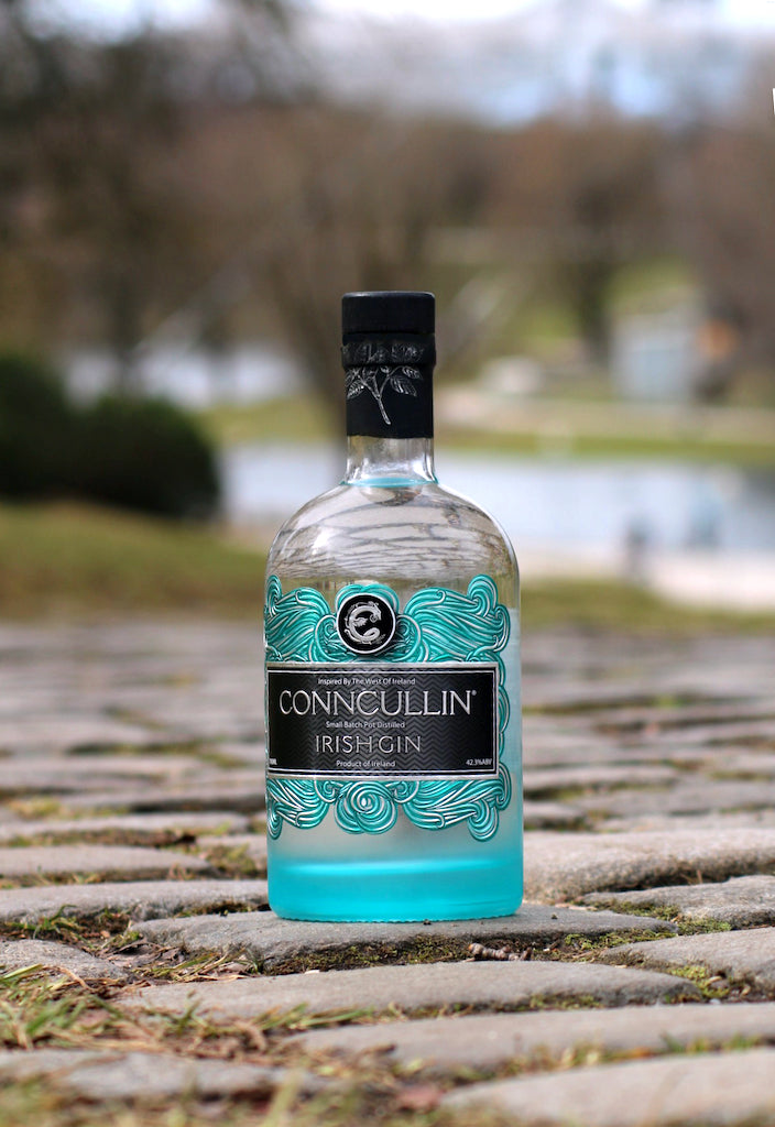 Conncullin Irish Gin Flasche mit türkisfarbenem Design steht auf einem gepflasterten Weg, im Hintergrund eine ruhige Parklandschaft.