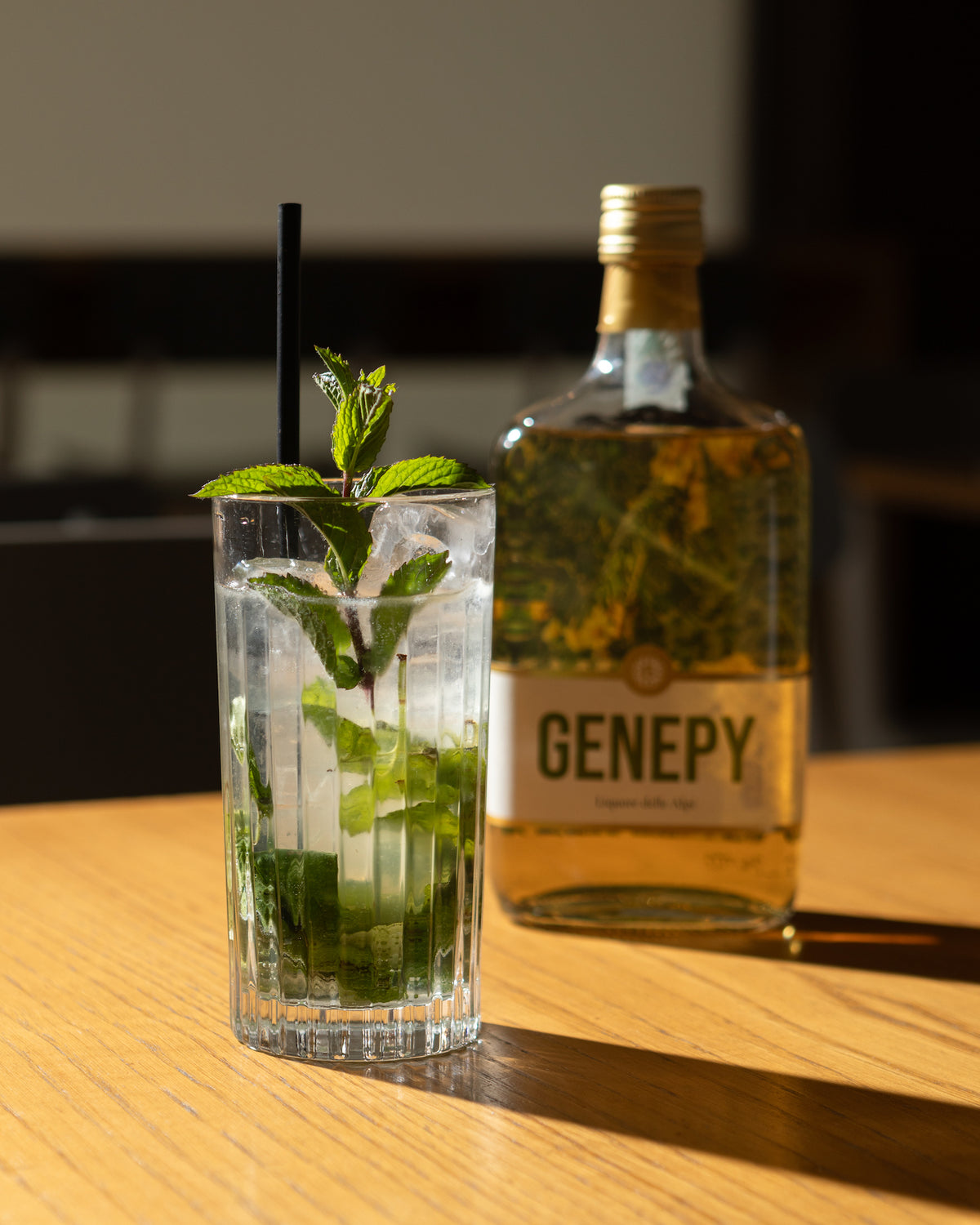 Glas Mojito mit frischer Minze und Eiswürfeln neben einer Flasche Genepy Fiori von Bordiga auf einem Holztisch.