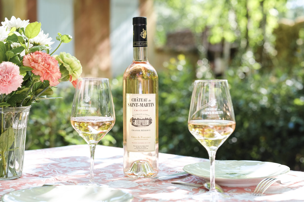 Château de Saint Martin Grande Réserve Rosé mit zwei Gläsern und Blumenstrauß auf gedecktem Tisch im Garten