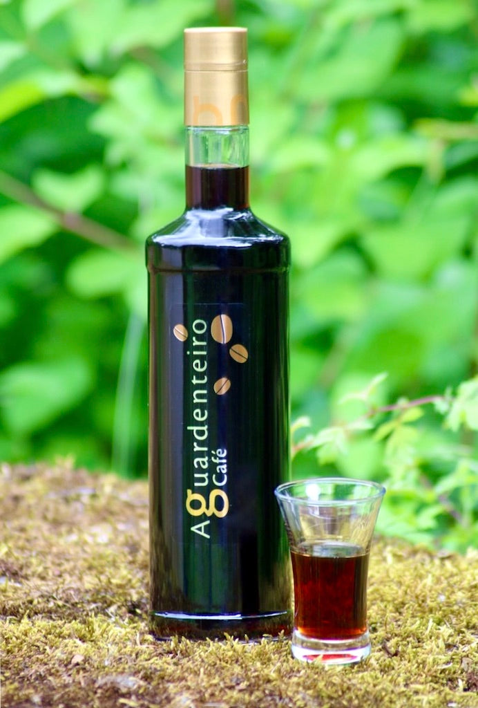 Flasche Aguardenteiro Café Kaffee Likör und ein Glas mit Likör vor grünem Hintergrund, auf moosbedeckter Oberfläche.