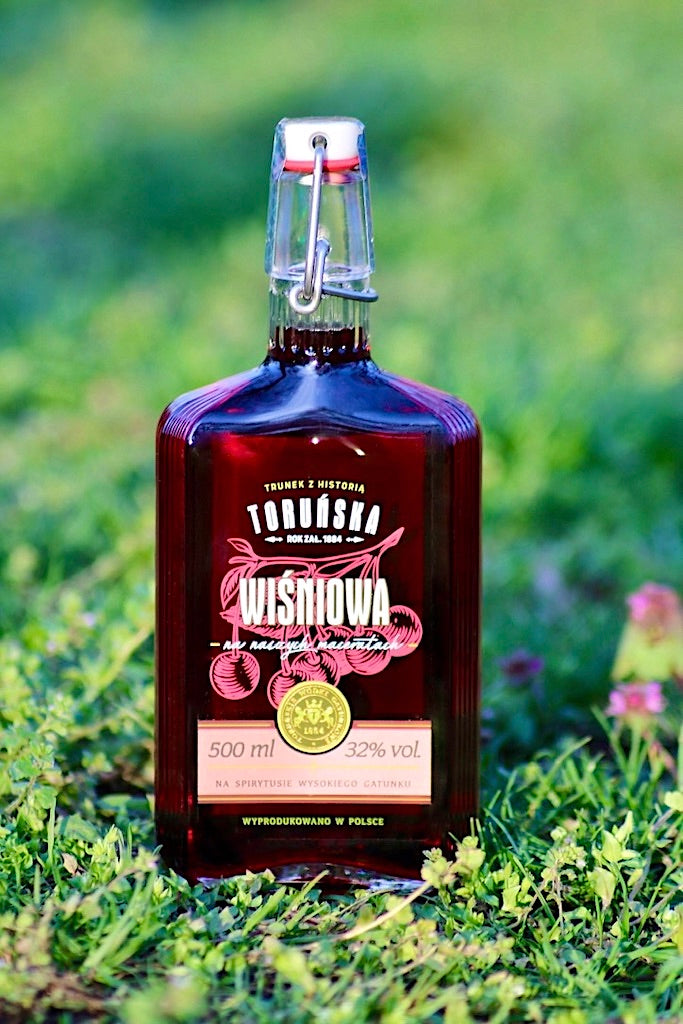 Flasche Toruńska Wiśniowa Kirschlikör, 500 ml, mit Bügelverschluss, arrangiert auf grünem Gras mit natürlichem Hintergrund.