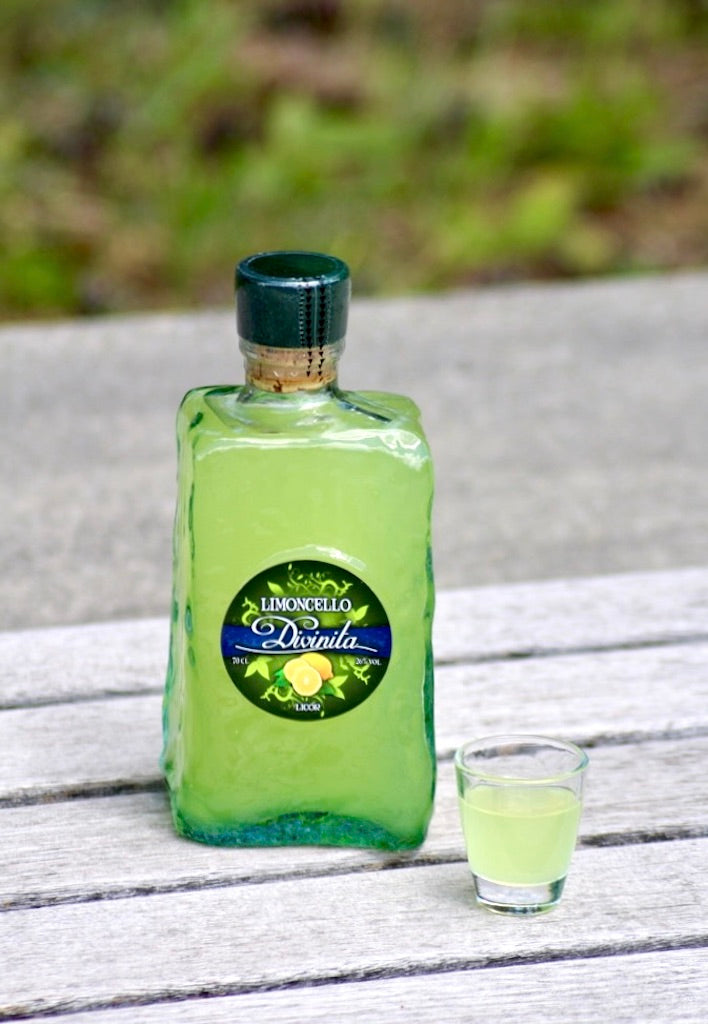 Limoncello Divinita Frasca Flasche auf Holztisch mit kleinem Glas und grünem Hintergrund