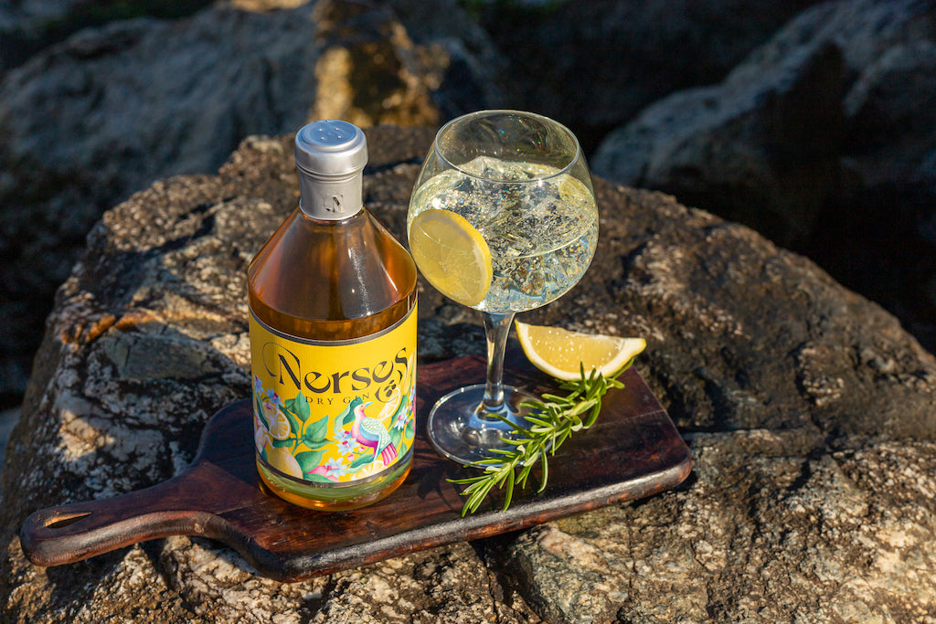 Nerses Dry Gin Flasche und Glas mit Zitronenscheibe und Rosmarin auf Holzbrett auf Felsen am Meer