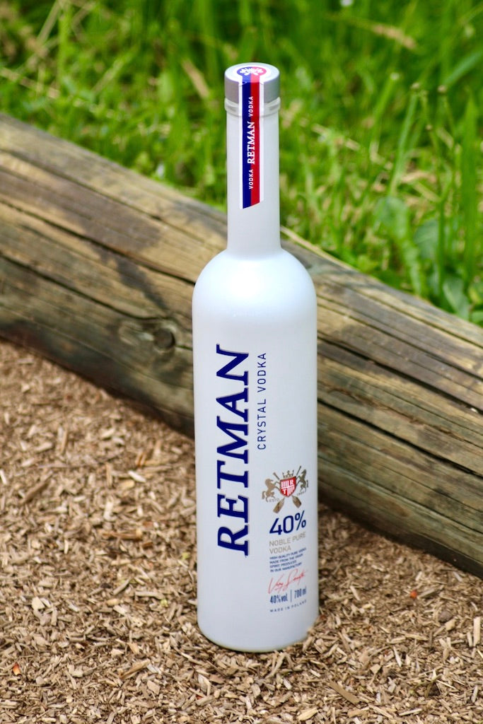 Retman Crystal Vodka Flasche auf Holzschnitzeln vor Gras und Holzbohle