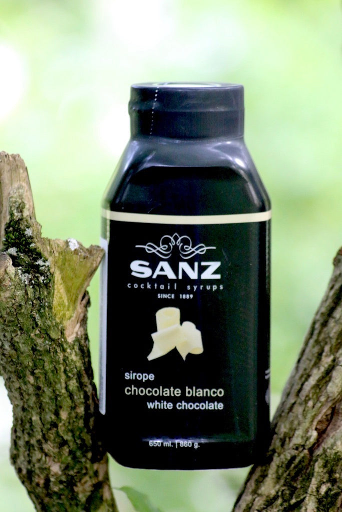Weiße Schokolade Sirup Sanz in schwarzer 650-ml-Flasche, platziert zwischen zwei Baumästen.