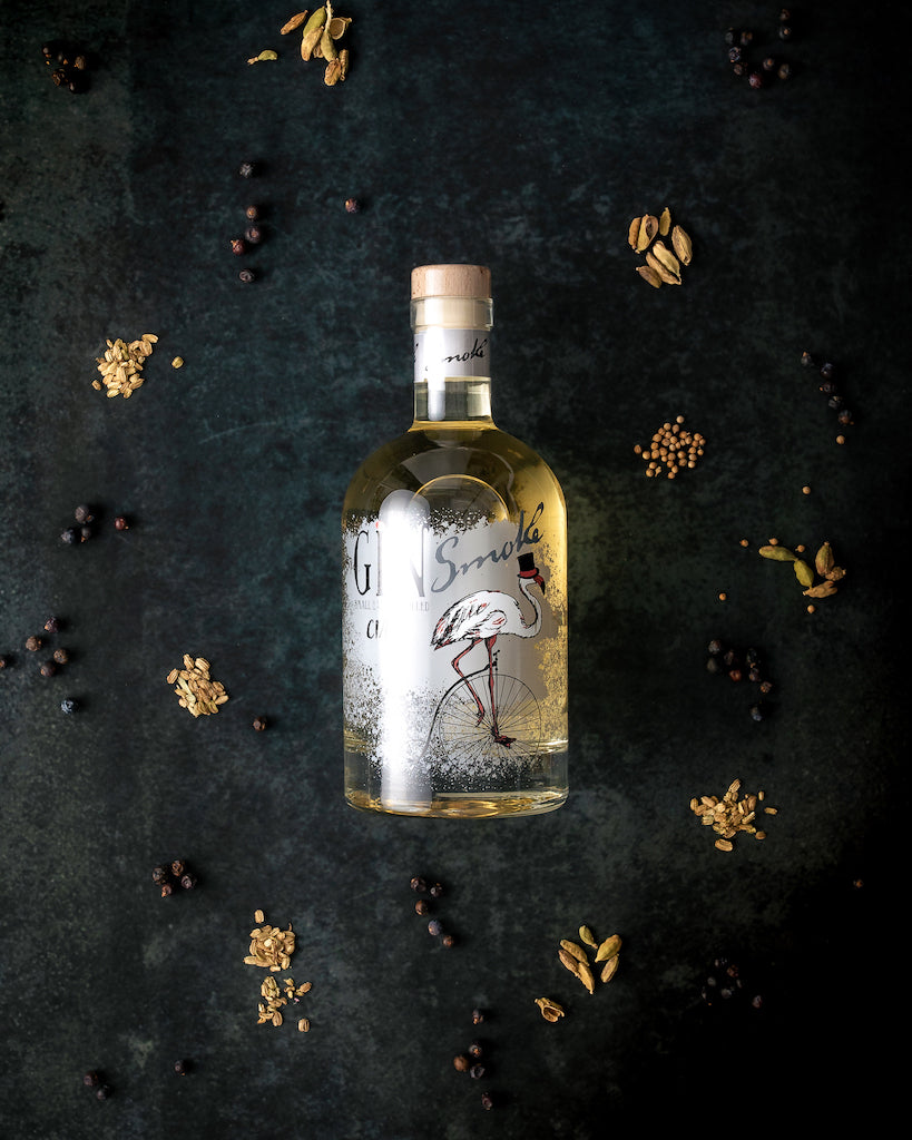 Flasche Ciais Gin Smoke von Bordiga auf dunklem Untergrund, umgeben von Botanicals wie Kardamom, Wacholder und Koriandersamen.