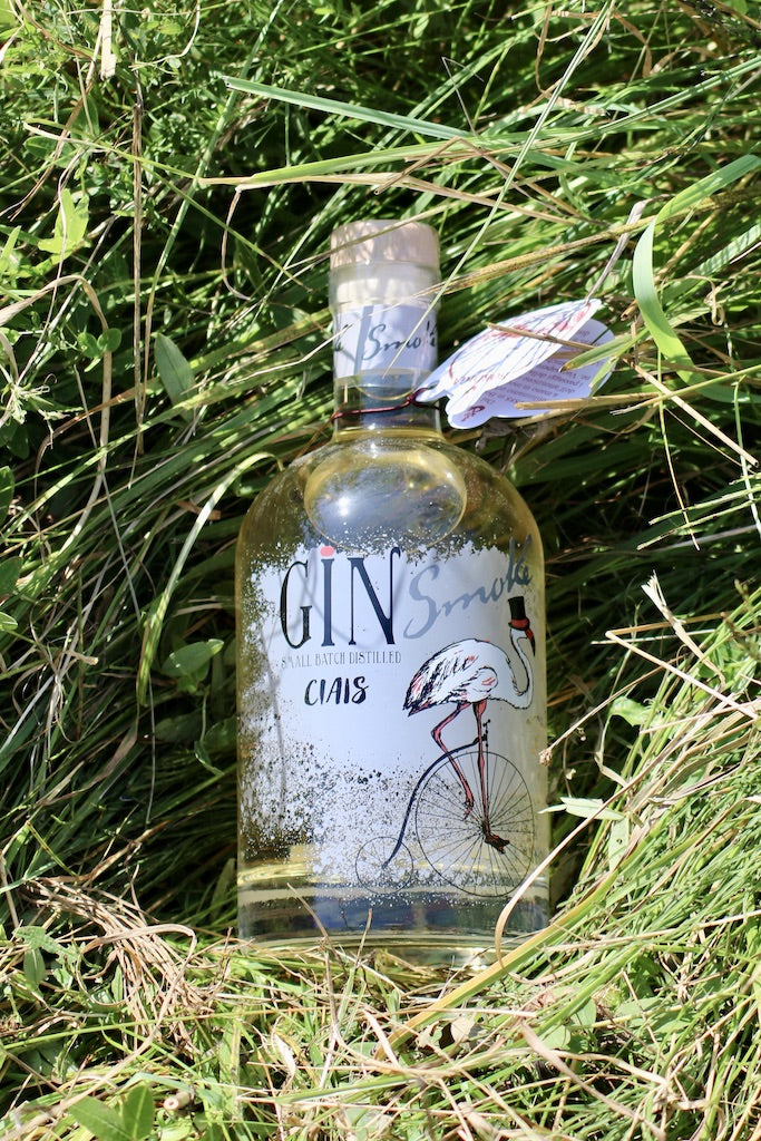 Flasche Ciais Gin Smoke von Bordiga mit Hangtag, liegend im hohen grünen Gras bei Sonnenlicht.