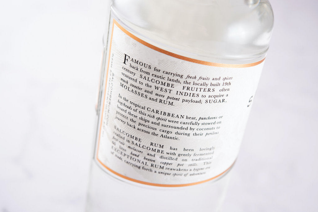 Rückseite der Salcombe Spiced White Rum Flasche mit einer Beschreibung der historischen Handelsrouten und der Rumherstellung.