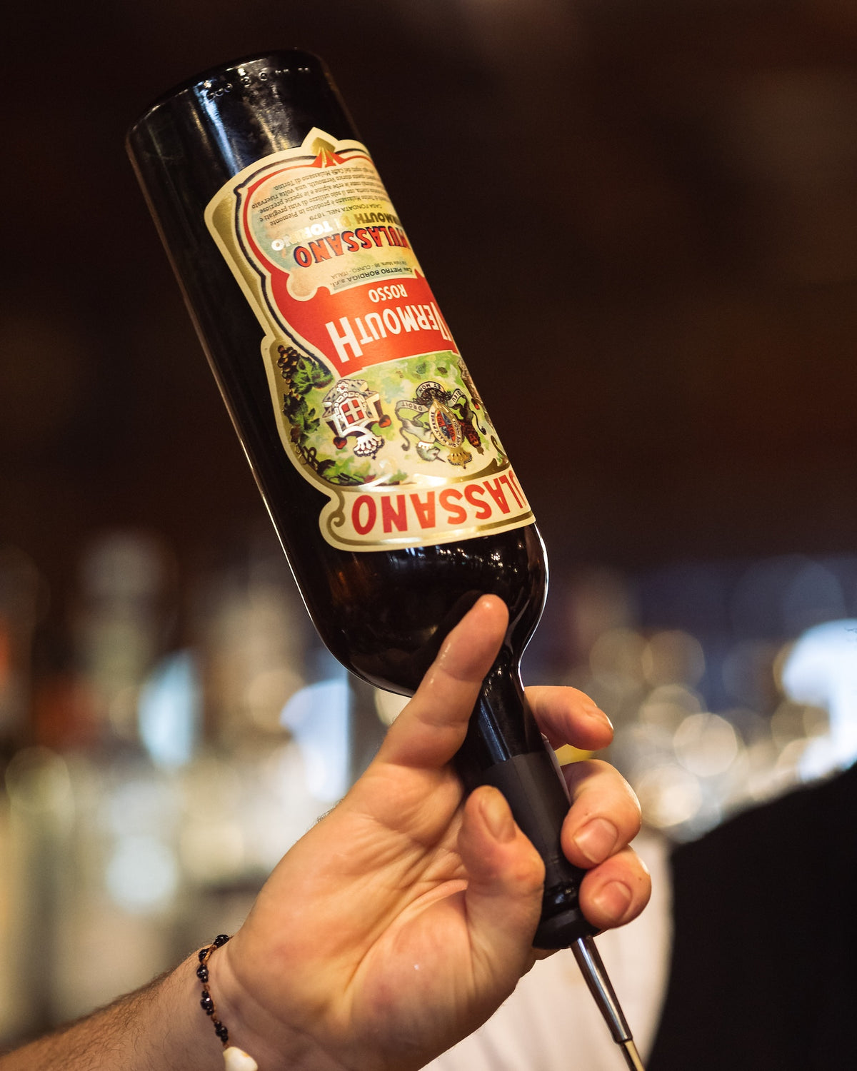 Vermouth di Torino Rosso Mulassano Flasche im Barsetting, gehalten von Barkeeper mit Ausgießer, unscharfer Hintergrund