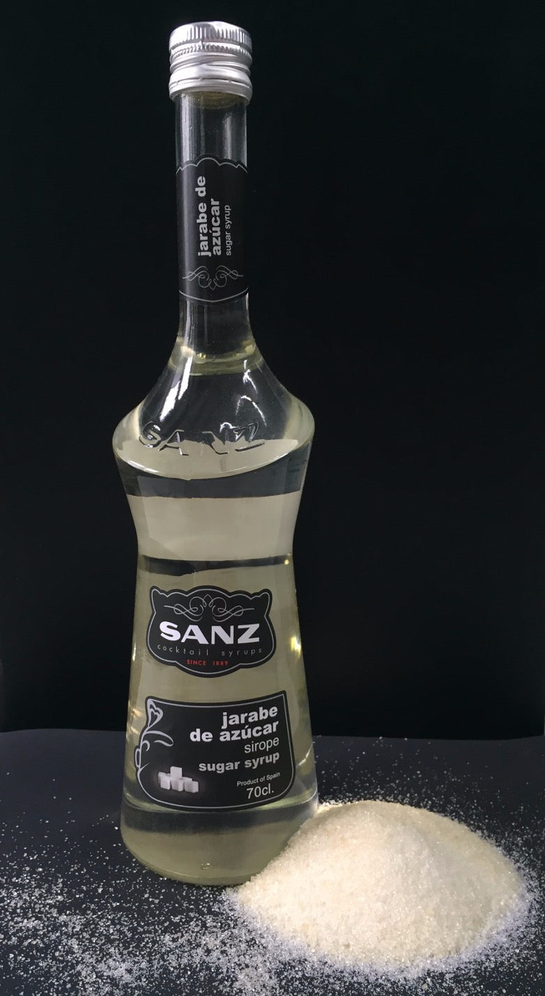 Flasche weißer Rohrzuckersirup von Sanz vor schwarzem Hintergrund, daneben ein Haufen kristalliner Zucker.