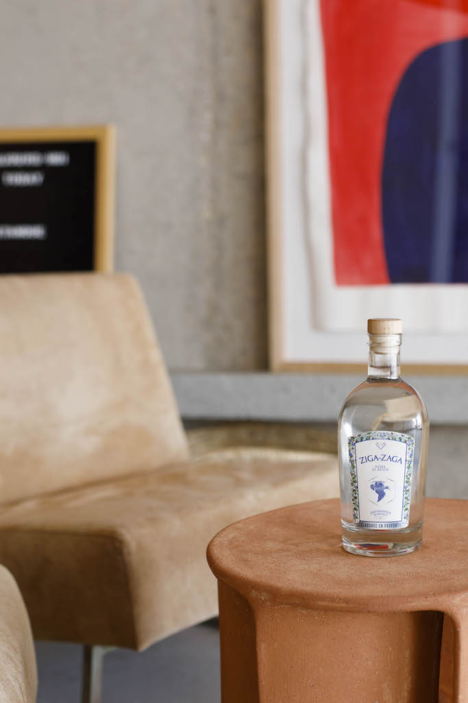 Flasche Ziga Zaga Vodka auf rundem Tisch, im Hintergrund beiger Sessel und modernes Kunstwerk an der Wand.