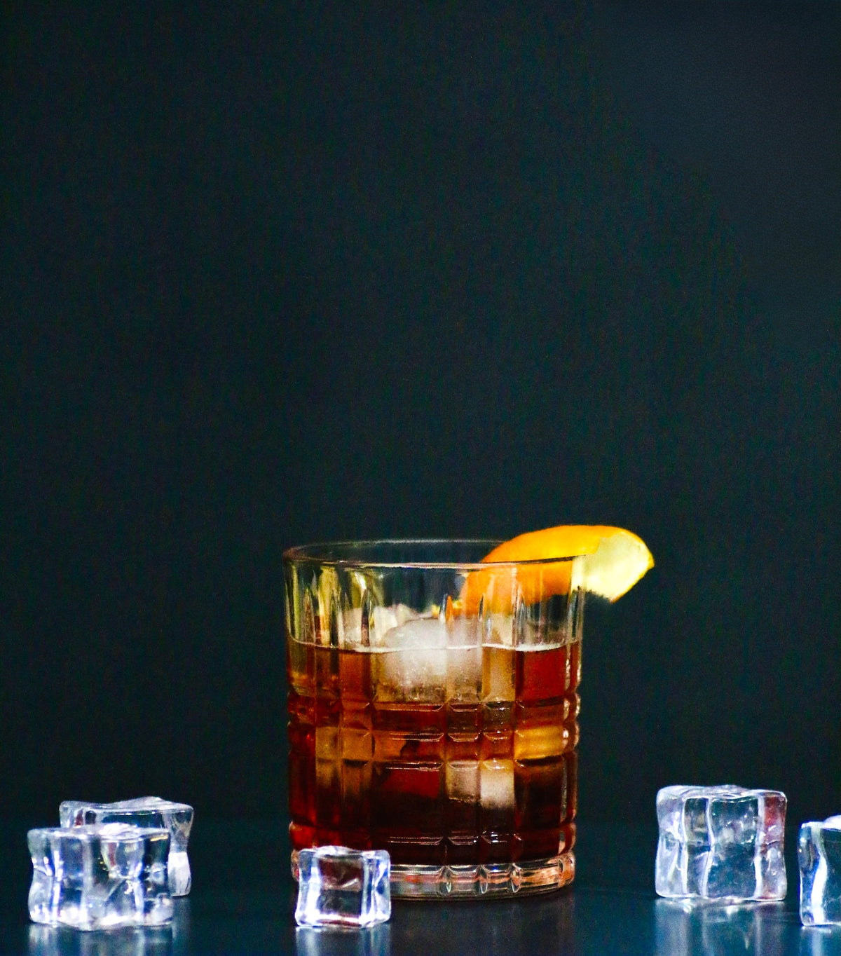 Amaretto Negroni im Rocks-Glas mit Eiswürfeln und Orangenzeste, serviert auf dunkler Oberfläche mit warmem Licht.
