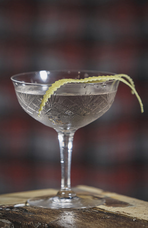 Atty Cocktail in einem Vintage-Cocktailglas mit eingraviertem Muster, garniert mit einer gedrehten Zitronenschale am Glasrand.