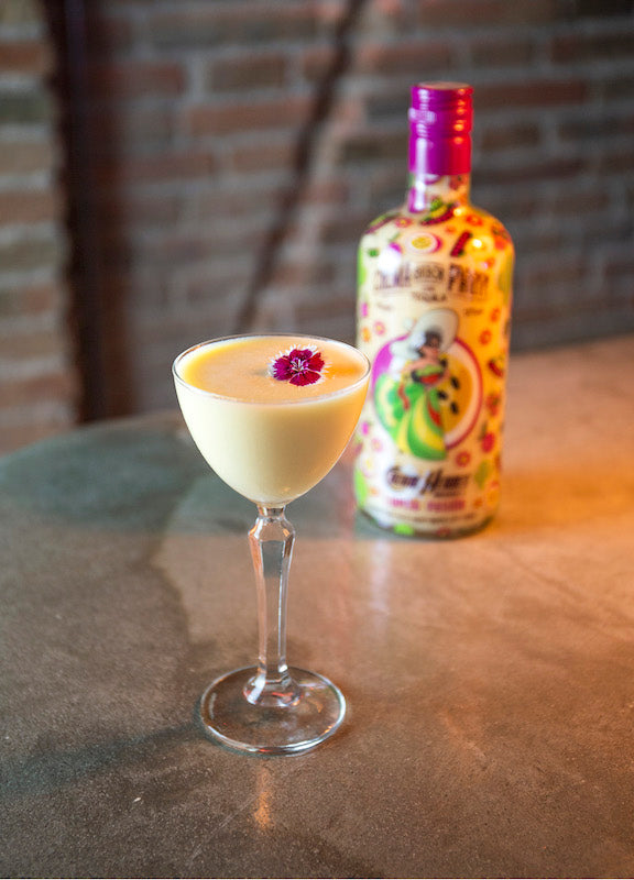 The Banana Lady Cocktail in Coupette mit Blüte, dahinter Lupita Pasión Flasche auf Bartresen