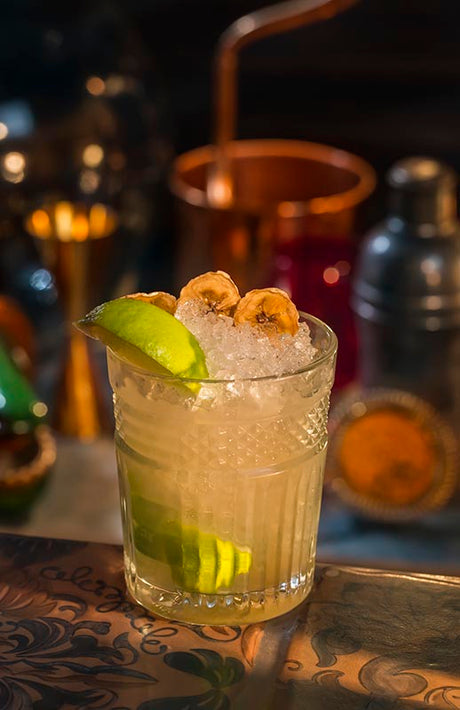 Bananen Guave Caipirinha mit Crushed Ice, Limette und Bananenchips vor Barhintergrund