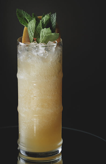 Big Bamboo Ya’ Cocktail in hohem Glas mit Crushed Ice, garniert mit frischer Minze und einer Scheibe exotischer Frucht.