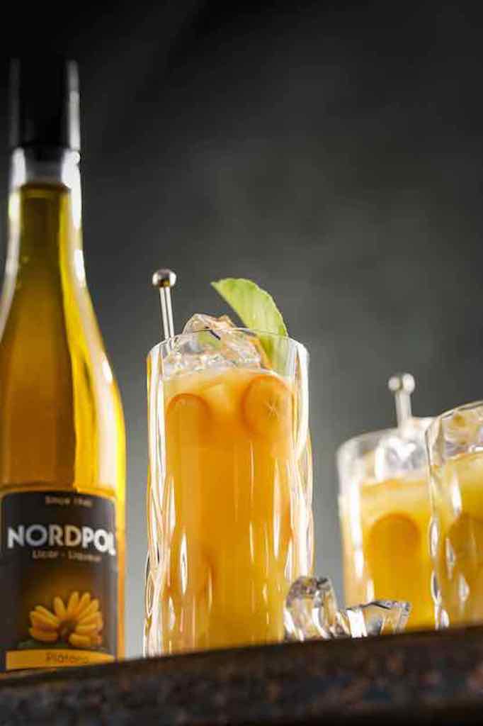Big Bird Cocktail mit Bananenlikör Nordpol, serviert auf Eis in einem hohen Glas mit Garnitur.