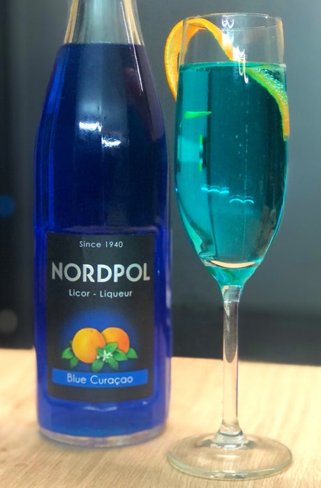 Blue Gin Fizz Cocktail im Glas mit Orange neben Flasche Blue Curacao Likör vor hellem Hintergrund