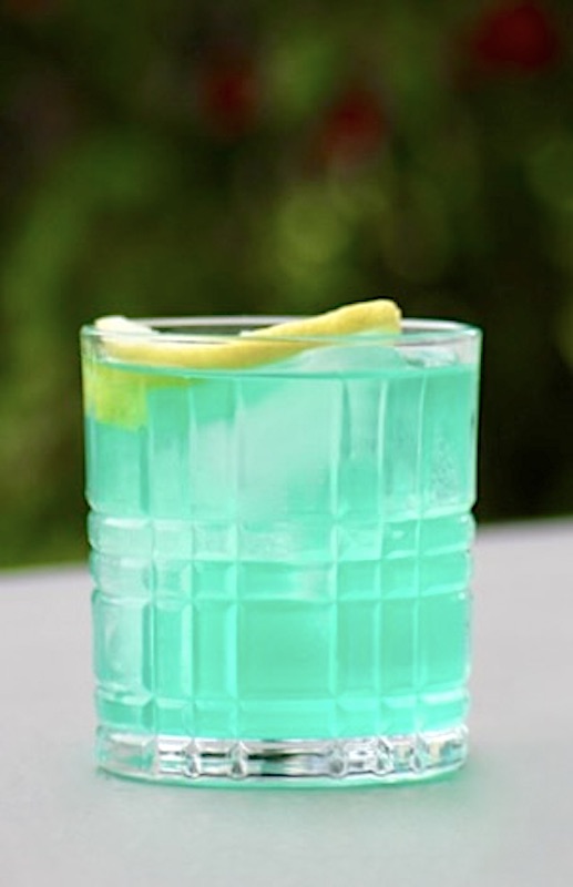 Ein erfrischender Blue Lagoon Twist Cocktail in einem Whisky-Glas, serviert mit Eiswürfeln und einer Zitronenscheibe als Garnitur. Der Cocktail hat eine leuchtend blaue Farbe und vermittelt tropisches Flair.