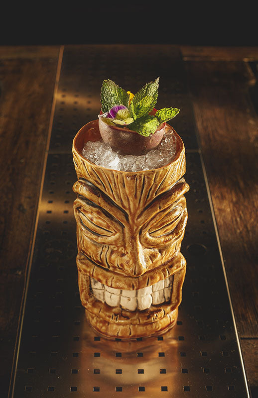 Bozarrón Cocktail im Tiki-Becher mit Crushed Ice, Passionsfrucht, Minze und essbarer Blüte als Garnitur.