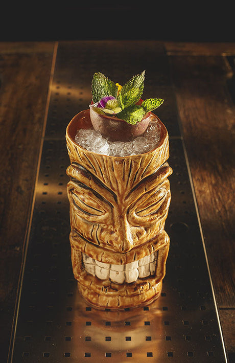Bozarrón Cocktail im Tiki-Becher mit Crushed Ice, Passionsfrucht, Minze und essbarer Blüte als Garnitur.