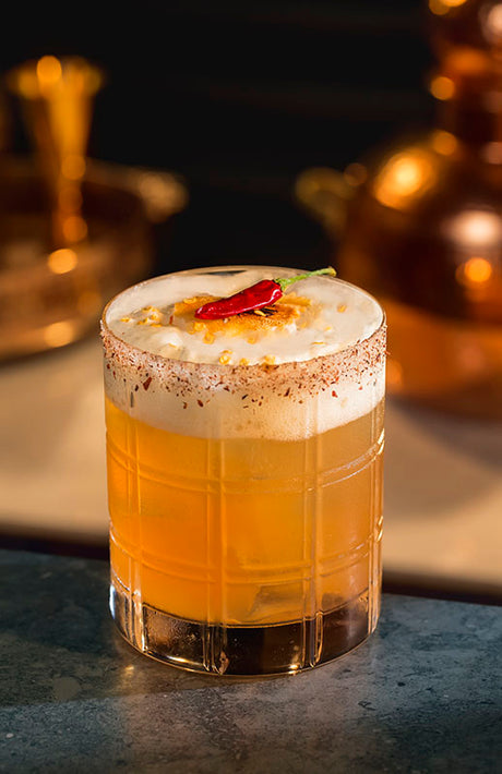 Camorra Margarita Cocktail im Rocks Glas mit Schaumschicht und Chili auf Bar vor warmem Hintergrund