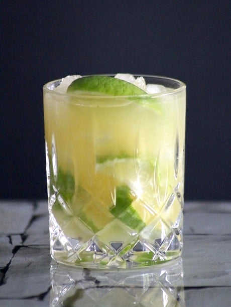 Caipiriña de piña Cocktail im Glas mit Ananasstücken, Limette und Crushed Ice auf dunklem Hintergrund