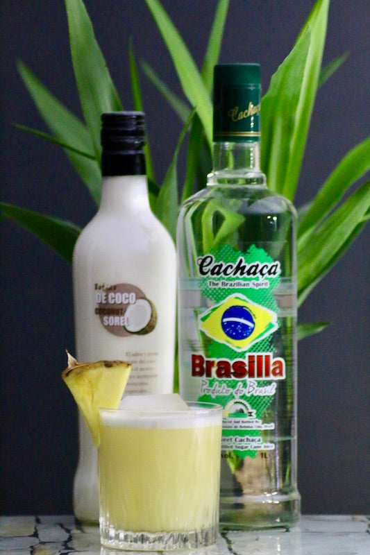 Cococabana Cocktail mit Cachaca Brasilla, Batida de Coco, Ananassaft und Ananasscheibe vor tropfengrünem Hintergrund