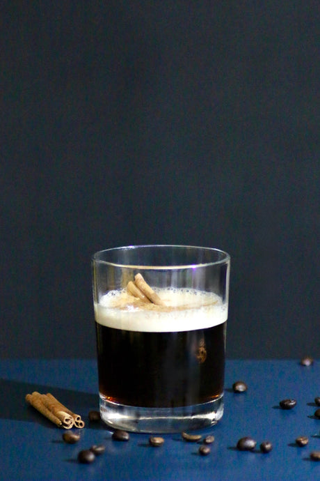 Coffee Shadow Cocktail in einem Rocks-Glas mit Zimtrinde und Kaffeebohnen als Dekoration auf dunklem Hintergrund.