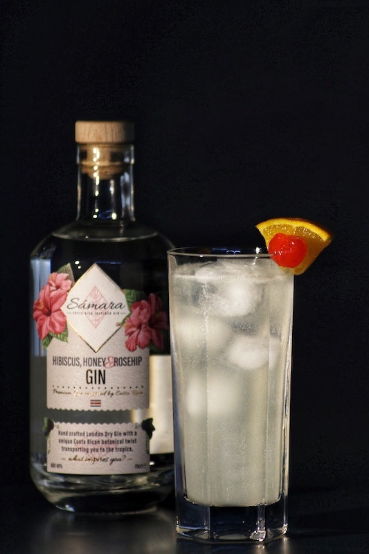 Colonel’s Big Opu Cocktail im Glas mit Eis, garniert mit Orange und Kirsche, Samara Gin Flasche im Hintergrund