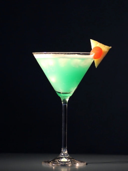 Envy Cocktail im Martini-Glas mit türkisgrüner Farbe und Ananasstück am Glasrand vor dunklem Hintergrund