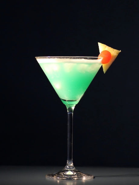 Envy Cocktail im Martini-Glas mit türkisgrüner Farbe und Ananasstück am Glasrand vor dunklem Hintergrund