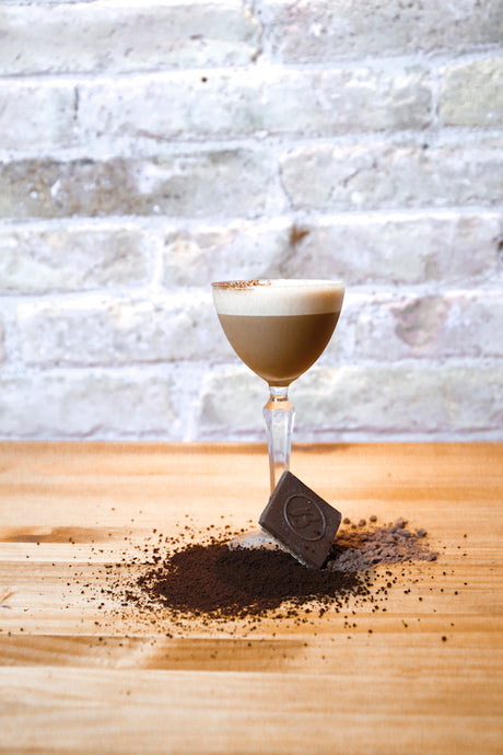 Fresón Strawberry Espresso Cocktail mit Schaumkrone, Kaffeepulver und Schokoladenstück auf Holztisch