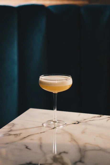 Gin Hass Cocktail in einer Coupette auf Marmortisch vor dunklem Hintergrund