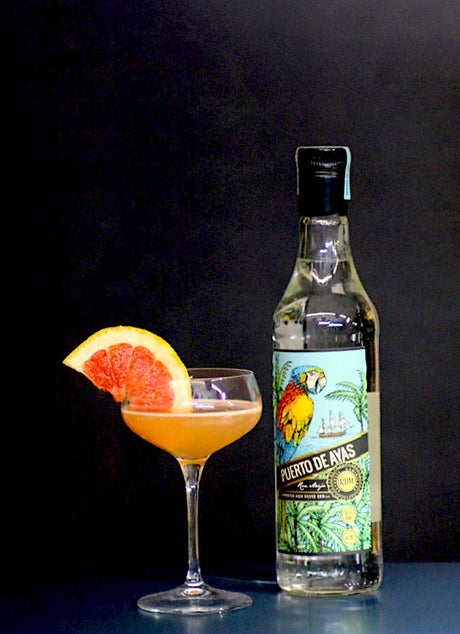 Grapefruit Daiquiri Cocktail im Cocktailglas mit Grapefruitscheibe, daneben eine Flasche Puerto de Avas Rum.