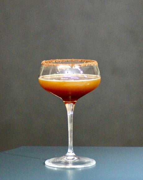 Anis Coffee Passion Cocktail im Martiniglas mit Schokoladenrand vor dunklem Hintergrund.