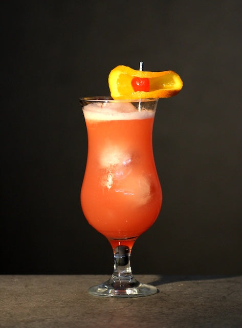 Hurricane Cocktail moderne Version im Curved-Glas mit Eis, orange-rot Farbe, garniert mit Orangenscheibe und Cocktailkirsche