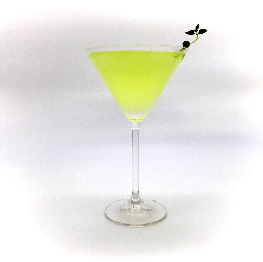 Krokodil Cocktail im Martini-Glas mit hellgrüner Farbe und kleiner Kräuterdekoration.