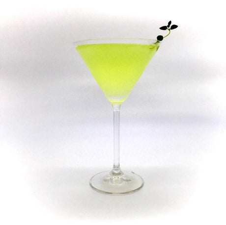 Krokodil Cocktail im Martini-Glas mit hellgrüner Farbe und kleiner Kräuterdekoration.