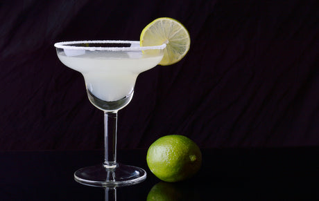 Heller Baudelaire Absinth-Cocktail in Margarita-Glas mit Salzrand und Limettenscheibe vor dunklem Hintergrund.
