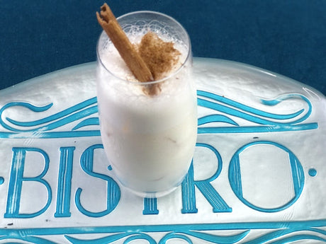 Leche de Pantera Cocktail in einem Glas, dekoriert mit Zimtstange und Zimtpulver, serviert auf einem Tablett mit Bistro-Aufschrift.