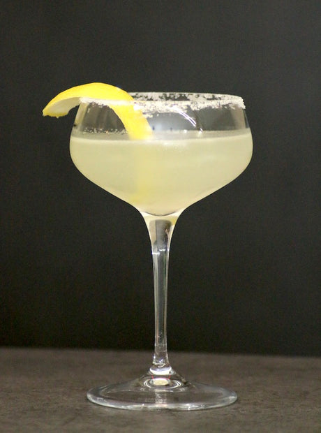 Lemon Drop Cocktail im Coupette Glas mit Zuckerrand und Zitronenzeste auf dunklem Hintergrund