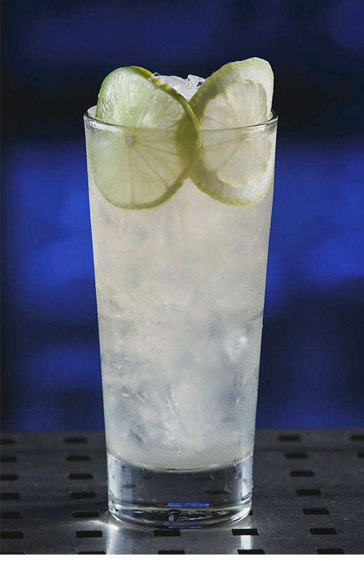 Lemonade Surprise Cocktail im Highball Glas mit Eis und Limettenscheiben vor blauem Hintergrund