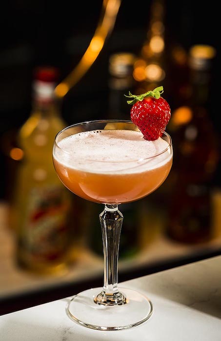 Erdbeer Margarita Cocktail im Glas mit Schaum und frischer Erdbeere als Dekoration vor Barhintergrund