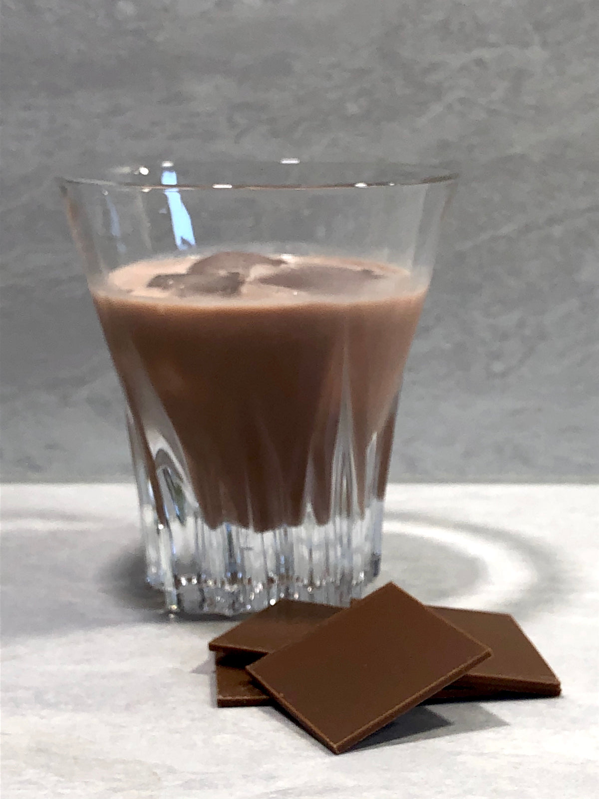 Medias de Seda Cocktail im Glas mit Eiswürfeln, davor Stücke dunkler Schokolade auf hellem Untergrund