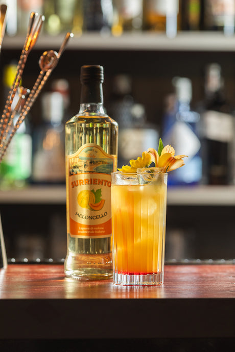 Meloncello Sour Cocktail mit Meloncello Surriento in einem Highballglas mit Eis und gelber Blüte als Dekoration.
