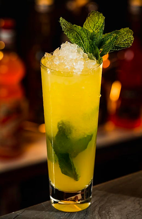 Mango-Ananas-Mojito im Highball-Glas mit Crushed Ice und frischer Minze vor Bar-Hintergrund