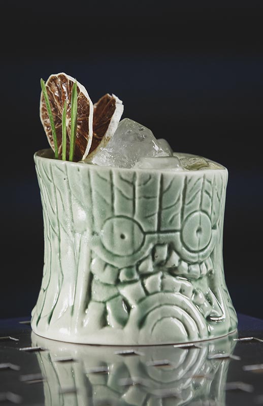 No Punch alkoholfreier Cocktail auf Eis in einem grünen Tiki-Becher mit Muster, garniert mit getrockneten Zitrusscheiben und Kräutern.